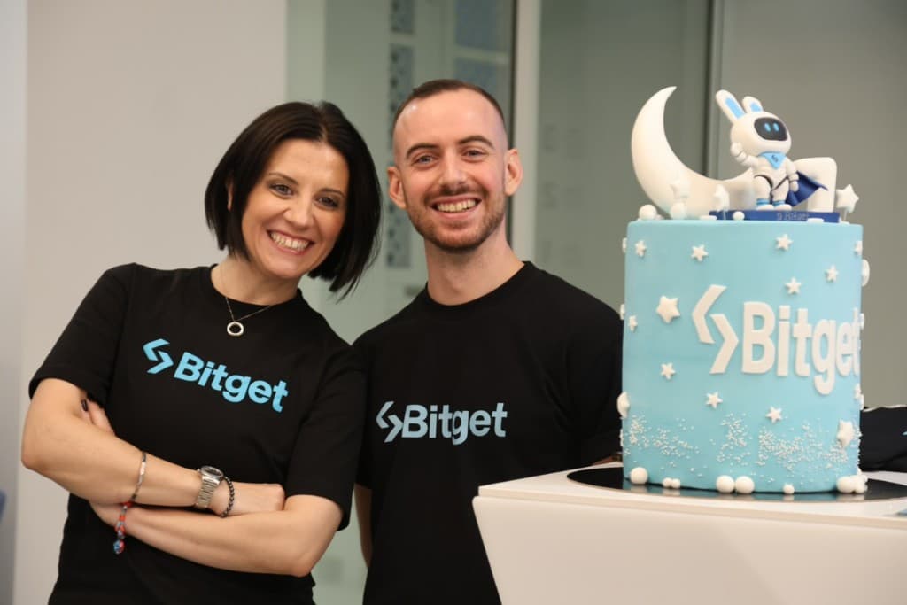 Two people beside a Bitget celebration cake at a gathering.