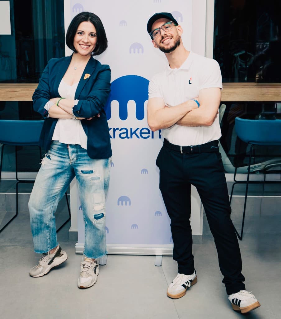 Two people in front of a Kraken backdrop at a live event.